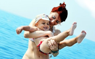 A mother playing with her baby standing in a sea