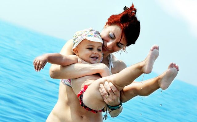 A smiling mother standing and holding her baby with the sea in the background