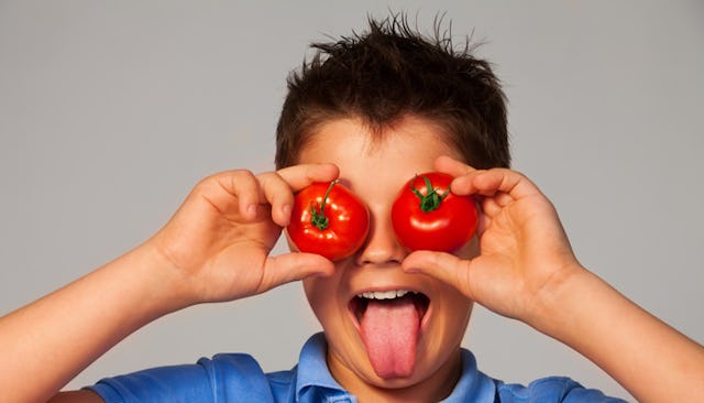 An 8-year-old boy holding tomatoes over his eyes and sticking out his tongue