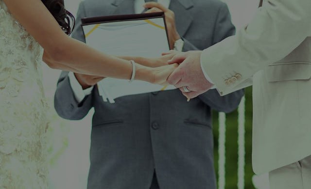 A bride in a white dress and a groom in a beige blazer holding hands and about to get married