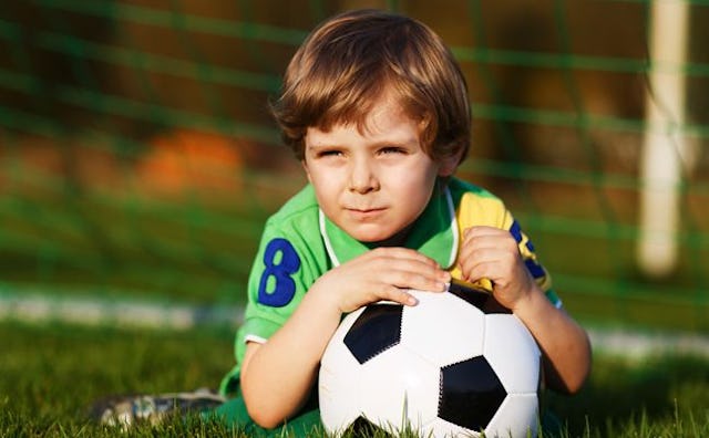 A brown haired boy wearing a green and yellow shirt with a dark blue number 8 on it lying on a socce...