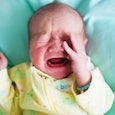 A baby crying on teal sheets in a yellow overall