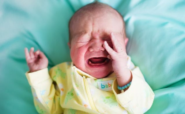 A baby crying on teal sheets in a yellow overall