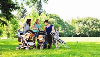 Three moms with strollers standing next to each other with their kids outside in a park