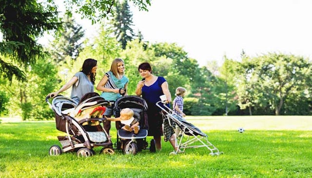 Three moms with strollers standing next to each other with their kids outside in a park
