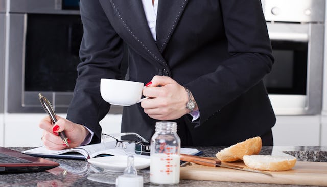 A mom in a black blazer, white shirt, and a watch is writing something down in a notebook on a messy...