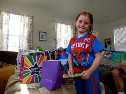 A little blonde girl wearing a Spiderman t-shirt while standing next to bags of presents 