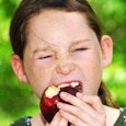 Girl with brown hair biting eating a red apple