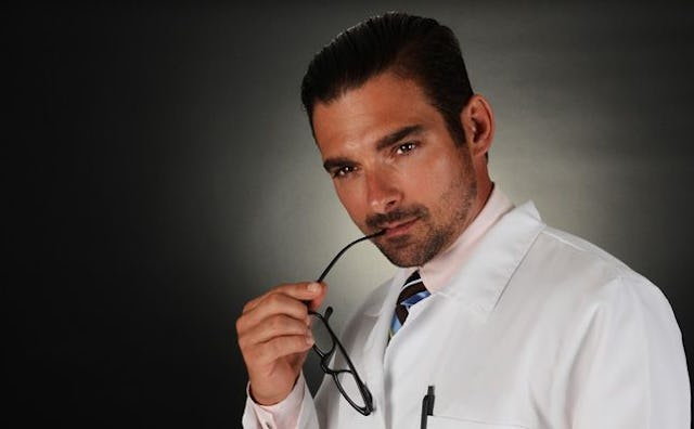 A gynecologist posing and holding glasses close to his mouth.