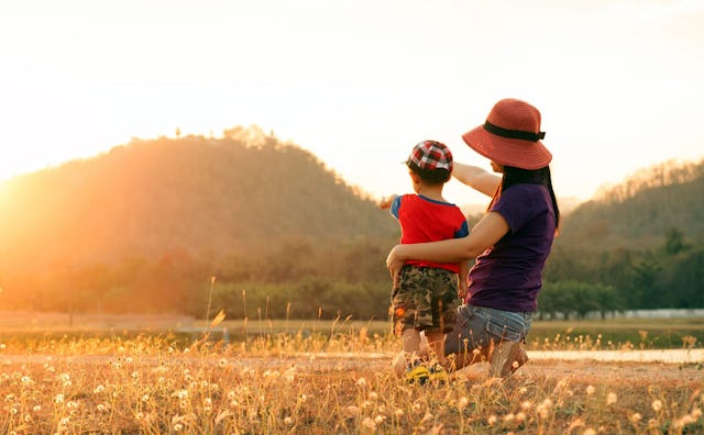 A mother holding her child and showing him an unknown object in the distance on a sunny day