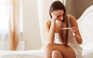 A woman holding a pregnancy test and stressed because she is going through intertility