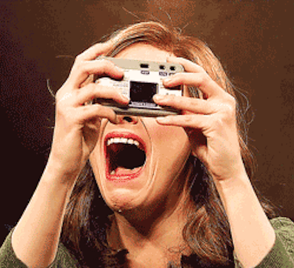 Gif of a red-haired woman wearing a green sweater and taking a photo of herself while crying