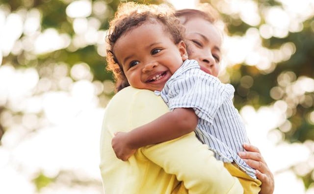 A mom in a yellow sweater holding her child who in a blue-white striped shirt