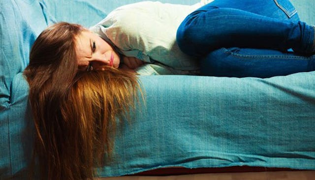 A woman lying curled up on a bed with a sad facial expression worrying about infertility