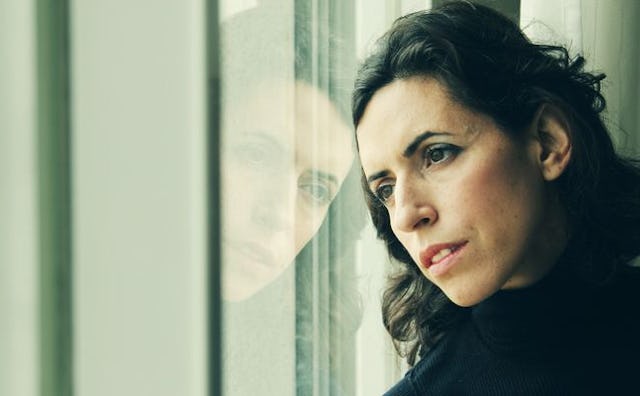 A dark-haired woman diagnosed with breast cancer looking through a window