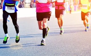 A close-up of four people running a marathon on a sunny day.