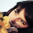 Close-up of a dark-haired, blue-eyed woman with bangs and a yellow flower next to her face after a m...