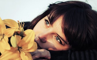 Close-up of a dark-haired, blue-eyed woman with bangs and a yellow flower next to her face after a m...