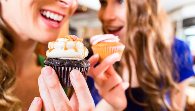 Two women holding cupcakes while smiling