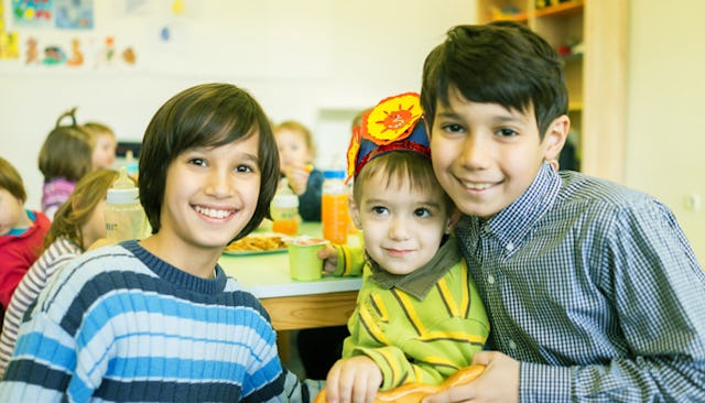 Three boys in a school posing for a photo while other kids are having a meal