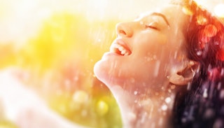 A woman smiling outside with rain falling all over her on a sunny day