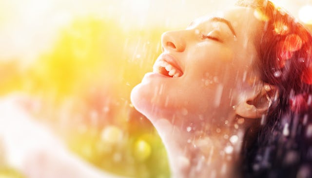 A woman smiling with her eyes closed during a sunny day while rain is falling at the same time