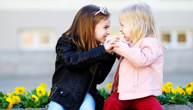 Blonde and brunette young girls sitting on a wall and pushing each other.