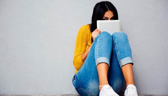 A young mother hiding her face with a notebook while sitting on a floor