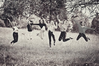 Six teenage girls happily jumping in a field surrounded by trees in black and white