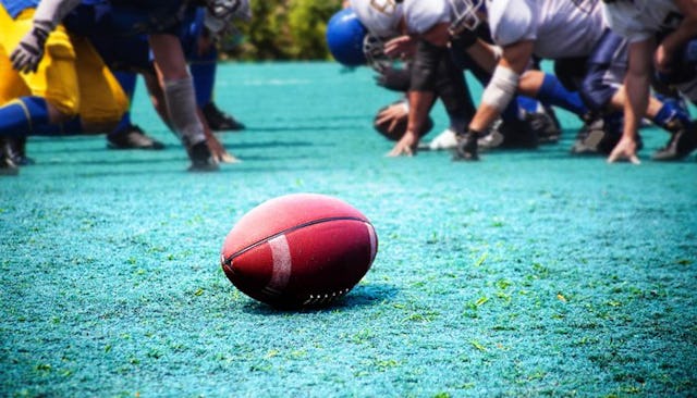 A bunch of people playing American football with the ball in the middle of the field