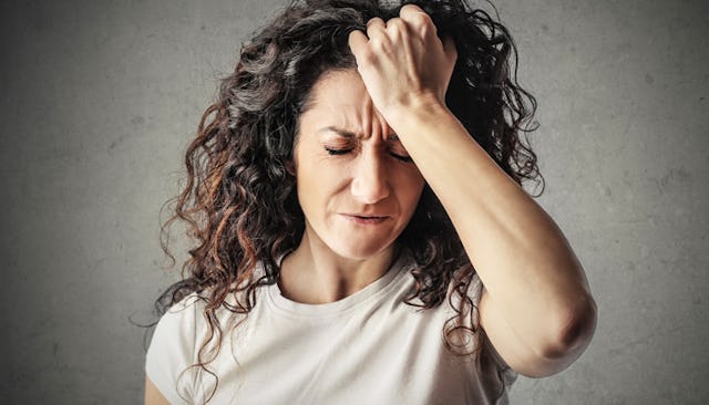 A black-haired woman holding her hair looking worried