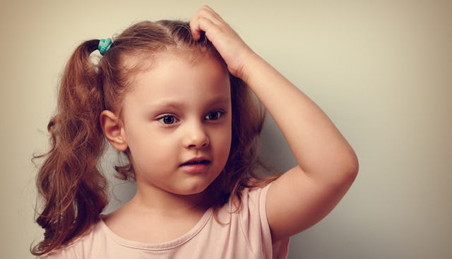 A curly-haired girl in a pink shirt looking confused and touching her hair.