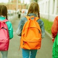 Three kids walking down a street wearing full pink, orange, and green backpacks 