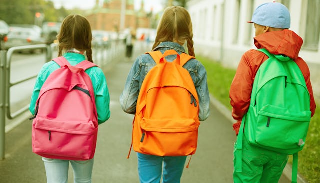 Three kids walking down a street wearing a pink, orange, and a green backpack