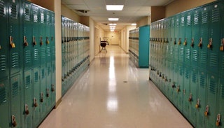 A high school hall with white floors and blue lockers on both sides, and lights on the ceiling