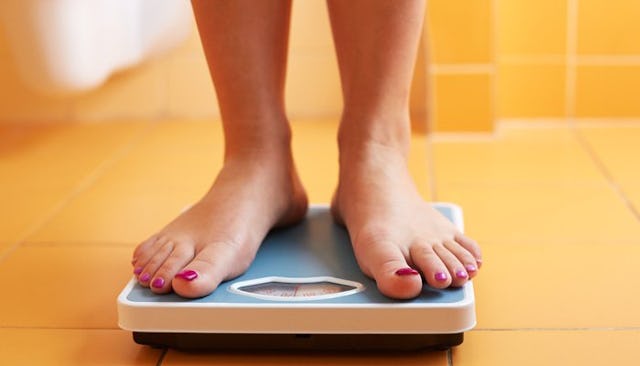 A person standing on a weight scale in a bathroom with orange tiles