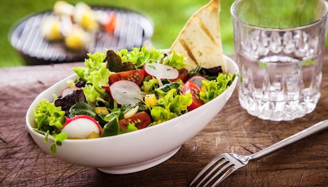 A prepared salad, served on a wooden table, with a glass of water next to it in a garden.