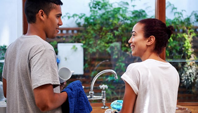 A married couple looking at each other smiling while washing the dishes