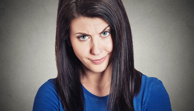 A woman in a blue shirt looking with one raised eyebrow, giving someone a stink eye