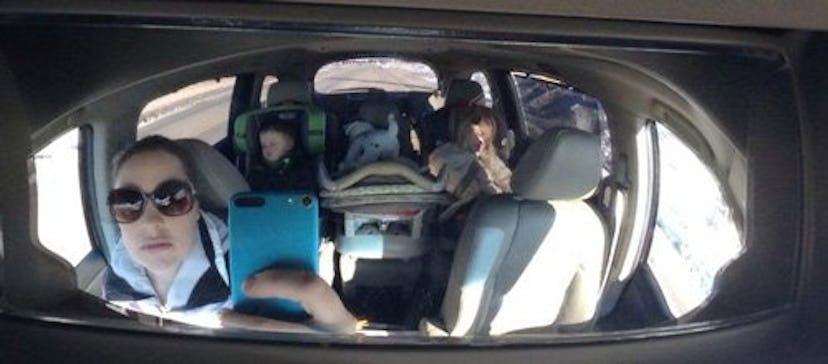 A mother taking a picture in the rearview mirror of her minivan with her kids behind