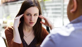 A woman in a brown shirt looking annoyed holding her hands on her head across from a man in a light ...