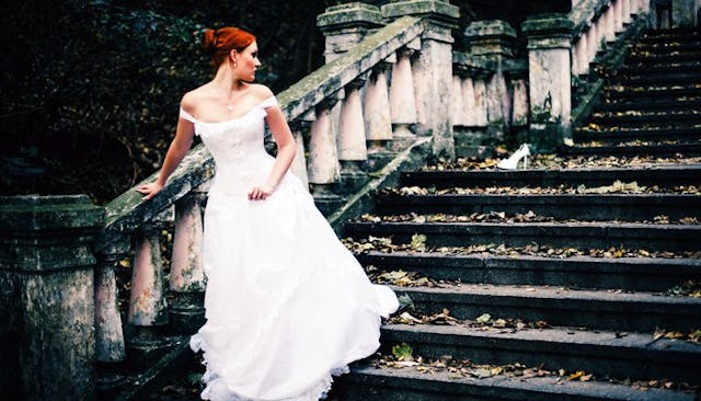 A red-haired young bride wearing a wedding dress while leaning on a stair handle