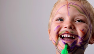 A little boy smiling with paint marks on his face from a colored pen