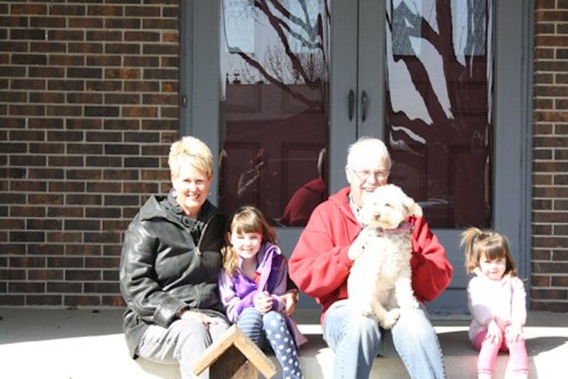 Two adults and two children sitting on a porch with a dog in man's lap.