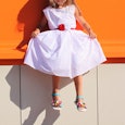 A girl in a white dress with red dots is sitting on an orange bench, who is experiencing sexism at s...