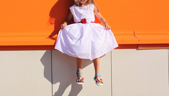 A girl in a white dress with red dots is sitting on an orange bench, who is experiencing sexism at s...