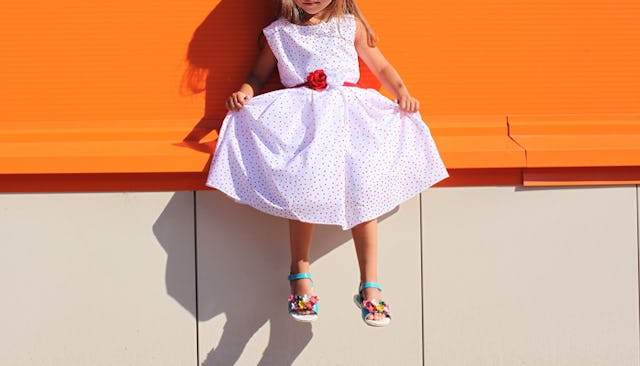 A girl in a white dress with red dots is sitting on an orange bench, who is experiencing sexism at s...
