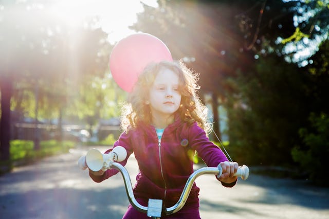 A girl riding a bike with a pink balloon in the background