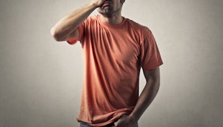A man in an orange T-shirt with one hand in his pocket and the other hand on his face regretting his...
