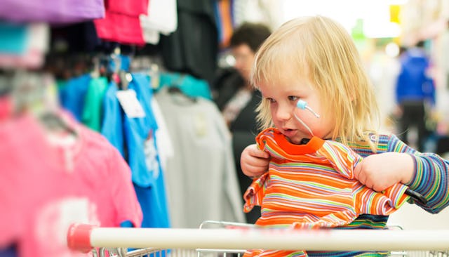 A little blonde girl trying on new clothes while sitting in a shopping cart